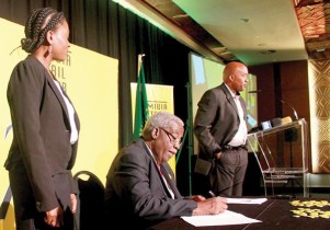 The Minister of Industrialisation, Trade and SME Development, Hon Immanuel Ngatjizeko signing the Namibian Retail Sector Charter witnessed by the CEO of the Namibia Trade Forum, Mrs Ndiitah Ngihipondoka-Robiati with Master of Ceremonies, Neville Basson hovering near the microphone.